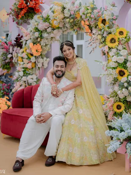 The couple shares a happy moment, seated together amidst the beautiful floral decor of their Haldi.