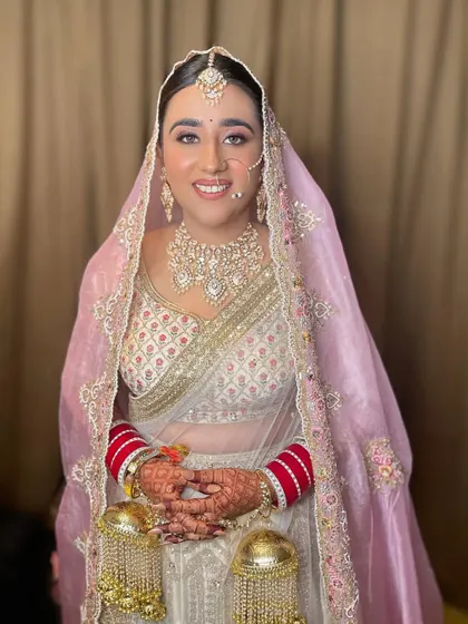 A full view of the bride in her white and gold lehenga with a soft pink dupatta, a unique and modern color combination.