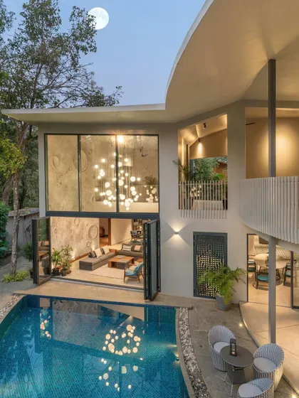 The Moon House at dusk, where the curved balconies and textured walls are reminiscent of lunar landscapes. The large, foldable glass doors open the living space completely to the pool, blurring the line between inside and out.