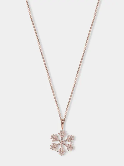 A delicate rose gold snowflake pendant necklace. The lighting is carefully controlled to make the small crystals sparkle.