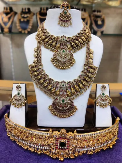 A heavy, antique-finish bridal set with intricate carvings and Kempu stones. This set includes a choker, haram, and a detailed temple vaddanam.