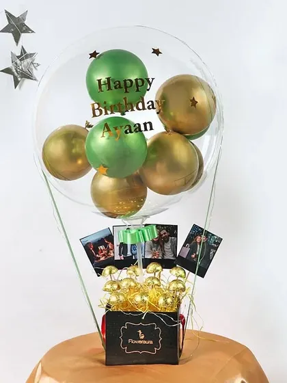 A creative hot air balloon-style bouquet. This gift includes a personalized clear balloon, a box filled with chocolates, and small photos hanging from the basket, making it a truly thoughtful present.