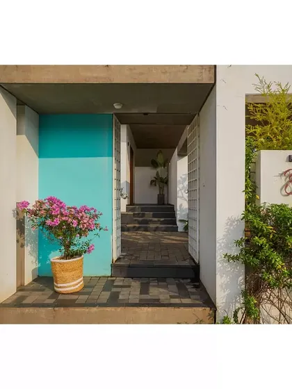 The entrance to the Aayi House is marked by a vibrant turquoise door, a playful counterpoint to the home's otherwise minimalist palette of white and exposed concrete. The name 'Aayi' is elegantly crafted in metal beside the door, a tribute to the home's matriarch.