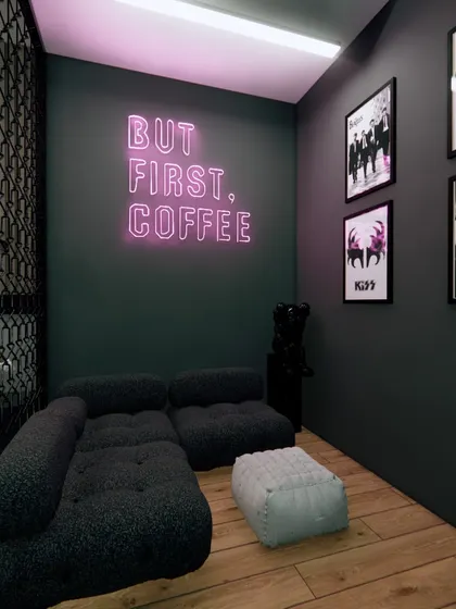A lounge area within the gaming room, featuring a 'But First, Coffee' neon sign and framed posters for a cool, edgy vibe.