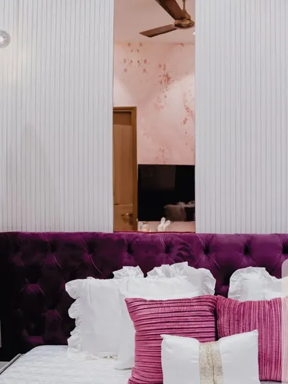A bedroom designed for a princess. The royal purple tufted headboard is the star of the show, complemented by pink pillows and soft, dreamy lighting. It's a real-life Barbie dream house.