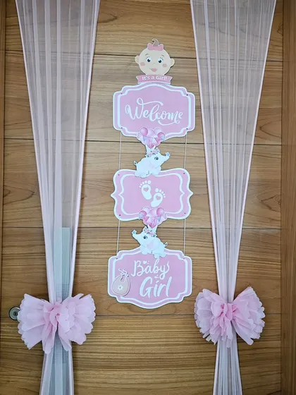A 'Welcome Baby Girl' door decoration. The pink signs, sheer curtains, and bows create a beautiful and delicate entrance to celebrate the new arrival.