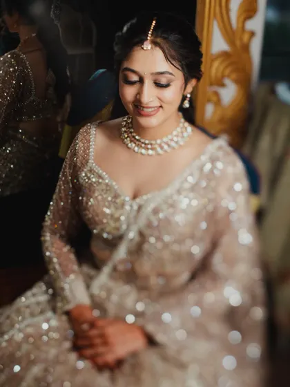 A smiling, seated portrait of the bride. Her hair is styled in a chic updo, and her makeup is glamorous, perfect for her sequined lehenga.