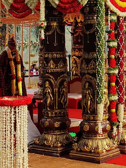 A detailed look at the ornate pillars of a temple-style mandap. The pillars feature carved figures and are wrapped in beautiful jasmine and rose garlands, showcasing our attention to traditional detail.