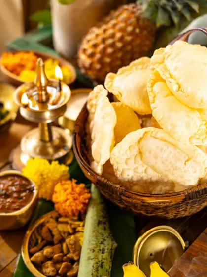 A festive arrangement of pappadams in a basket, surrounded by other Onam delicacies and a lit vilakku.
