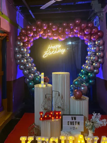 A first birthday decoration done in a home setting. We used a multi-color chrome balloon arch, ribbed stands, and marquee letters for the name 'KRISHNAYA' to create a festive photo corner.