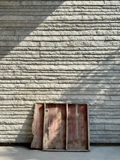 A work-in-progress shot showing a section of formwork used for concrete, resting against a newly completed wall of hand-chiseled stone. This image captures the two materials that are central to our practice: the raw and the crafted.