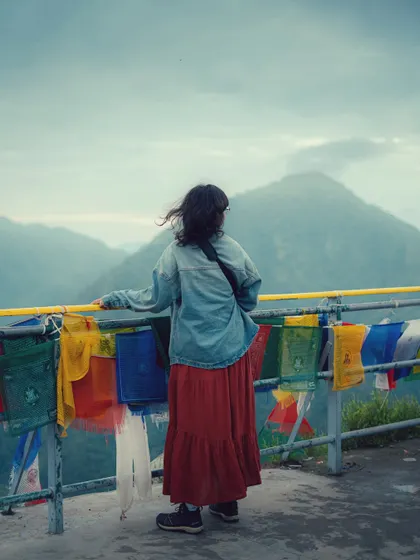 A portrait of me enjoying the view at Dalai Hills, surrounded by colorful Tibetan prayer flags and the vast mountain landscape.