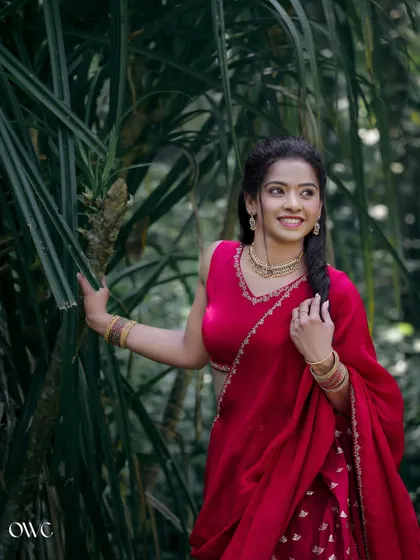 A candid portrait of the bride-to-be in a red lehenga, smiling as she interacts with her natural surroundings.