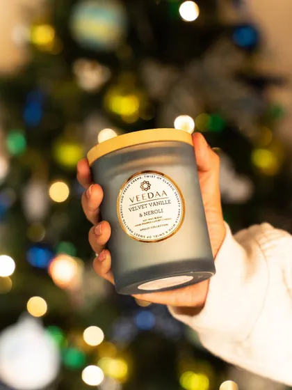 The warmth of our Velvet Vanille & Neroli candle, held against the festive backdrop of a Christmas tree. This fragrance is a cozy and comforting choice for the holiday season.