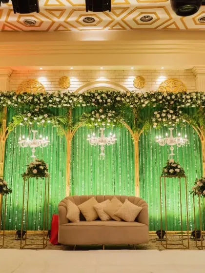 This reception stage combines a lush green backdrop with elegant golden arches and sparkling chandeliers. The design creates a feeling of an enchanted forest, perfect for a magical evening celebration.