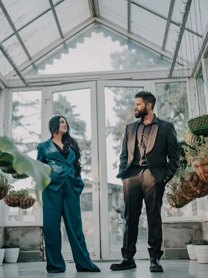 A stylish, full-length portrait of the couple in a modern glasshouse. The composition emphasizes their fashion-forward look against the unique architecture, perfect for a chic mountain pre-wedding shoot.