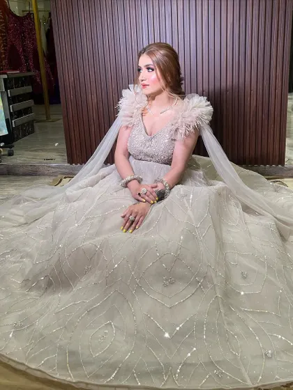 A seated portrait in our beige bustier ball gown. The shimmer tulle fabric, embellished bodice, and dramatic feather and ruffle sleeves create a look of pure luxury and sophistication.