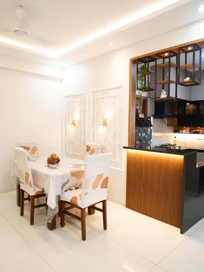 An elegant dining area adjacent to an open kitchen with a breakfast bar. The wall features decorative molding and sconce lighting for a classic touch.