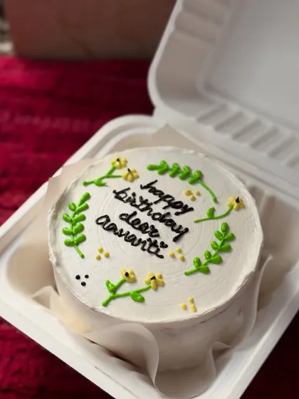 A beautiful and minimal birthday cake with delicate greenery and tiny yellow flowers piped around the message "happy birthday dear Aavanti."