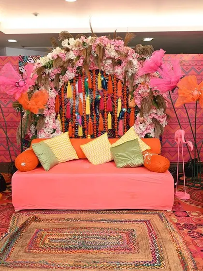 A full view of the vibrant Mehendi stage setup. I used a rich, patterned backdrop, a comfortable diwan, and colourful props like floral umbrellas and flamingo figures to create a lively, bohemian vibe.