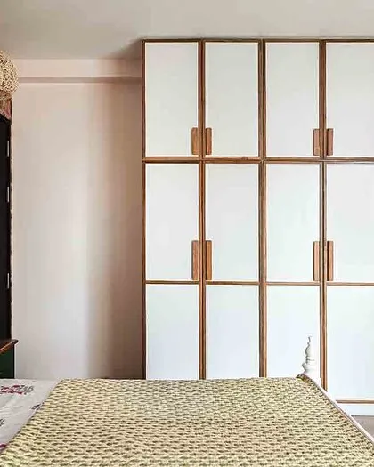 A guest room with bold pink wallpaper and a custom white wardrobe with teak wood trim and handles.