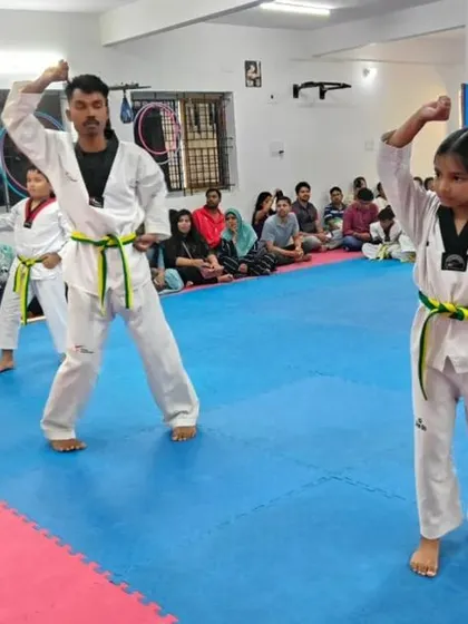 An instructor demonstrates a high block alongside a young student.