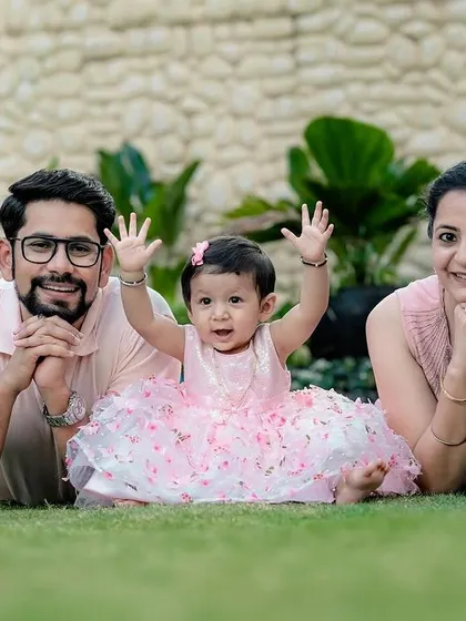 Such a happy moment. This little girl's joyful expression with her hands up, framed by her loving parents, makes for a perfect outdoor family photograph on the grass.