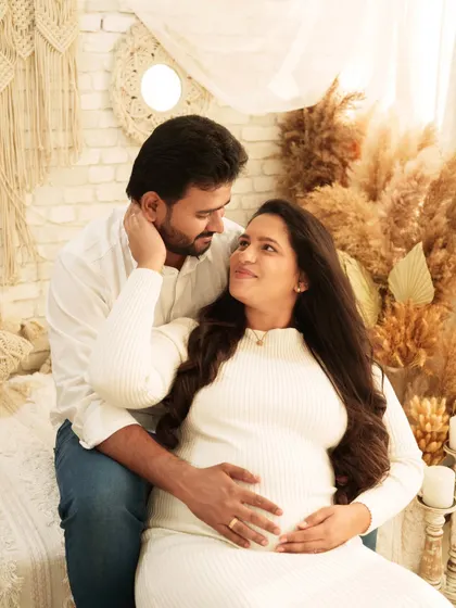 An intimate couple's portrait filled with affection. The couple sits together on a bed in a boho-chic setting, looking into each other's eyes with loving smiles.