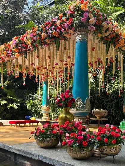 This colorful mandap with turquoise pillars and a canopy of fresh flowers creates a vibrant and joyful setting for a daytime wedding.