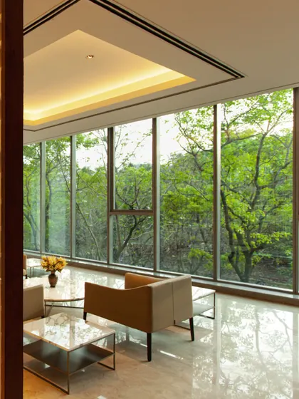 A lounge area at the Amara Raja campus, where floor-to-ceiling windows frame a view of the dense surrounding forest. This is a prime example of our biophilic approach, where the building is designed to feel like a part of the landscape.
