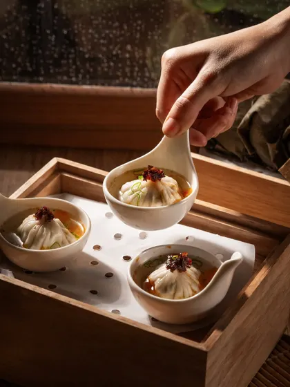 Soup dumplings (xiao long bao) served in individual spoons. This action shot captures the moment of serving, highlighting the delicate nature of the dish.