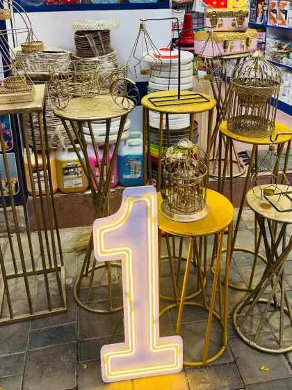 I offer a wide range of party props for rent to complete your event's look. This photo shows some of my inventory, including gold-finished cake stands, decorative plinths, and a large light-up number '1', perfect for first birthdays or anniversaries.