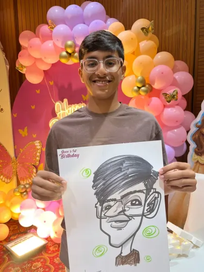 A young guest at a birthday party with a colorful balloon backdrop, holding his new caricature.