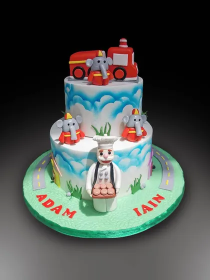 A fun, two-tiered cake featuring Dumbo the flying elephant. This whimsical design includes a little baker and a road circling the base, perfect for a child's party.