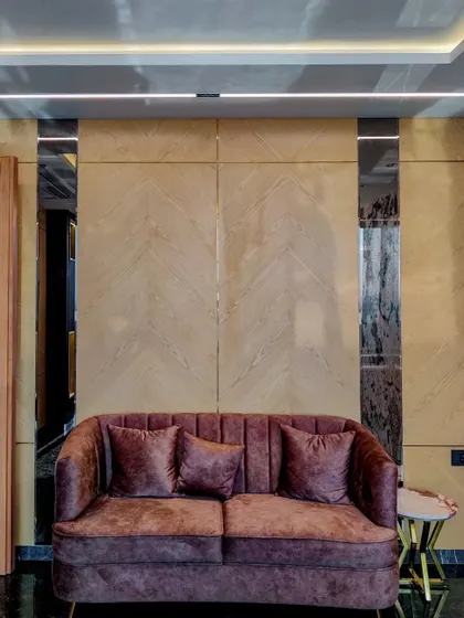 A full view of the seating area in Mr. Sameer's cabin, featuring a plum-colored sofa against a wall of light wood veneer and mirrored strips. The design creates a comfortable yet formal space for discussions.