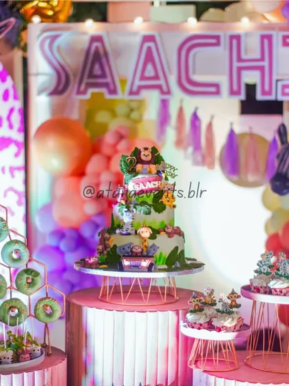 The dessert station at a wild jungle-themed birthday party. The cake is adorned with jungle animals, and the table is filled with themed treats like green-frosted donuts.