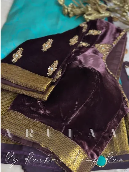 A rich plum-colored velvet blouse with scattered floral butis. The saree's original zari border is used to create a beautiful contrast at the hem and cuffs.