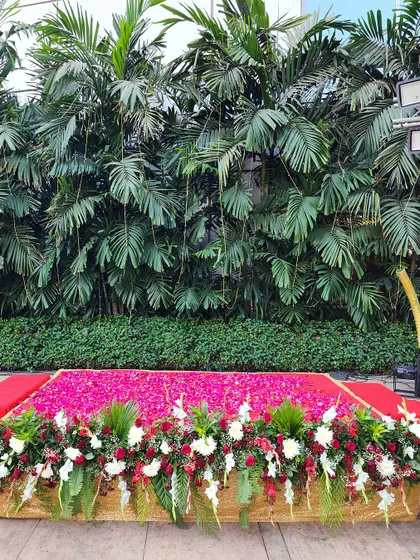 A simple yet impactful stage decoration with a bed of vibrant pink rose petals, bordered by red and white flowers against a lush green backdrop.