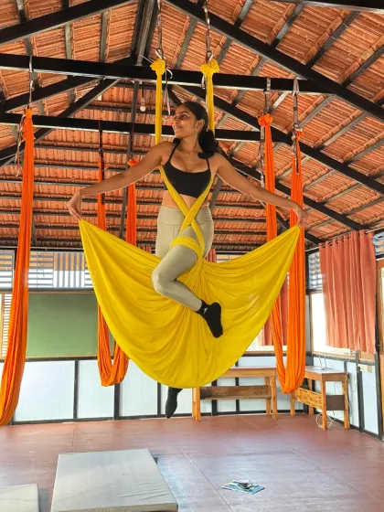 A student radiates joy and confidence while posing in the yellow aerial hammock, wrapped in the supportive silk.
