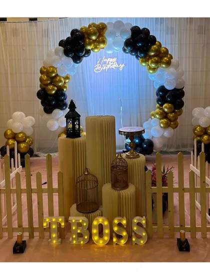 A stylish black, white, and gold themed party setup, featuring a circular balloon arch and "BOSS" marquee letters.