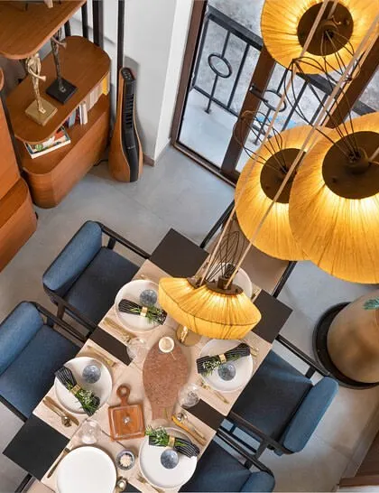 An aerial view of the dining area, highlighting the dramatic double-height ceiling. A cluster of large, dandelion-inspired pendant lights creates a stunning focal point over the dining table, adding warmth and a touch of whimsy to the space.