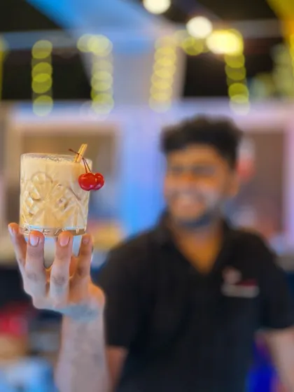 A beautifully crafted cocktail, held up by our bartender. The focus is on the drink itself: the crystal-clear ice, the perfect dilution, and the simple yet elegant cherry garnish.