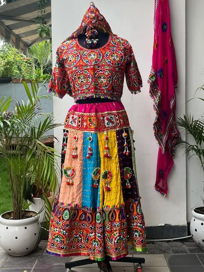 This mannequin displays a stunning multi-colored chaniya choli with a red blouse and pink dupatta, showcasing the vibrant patchwork and tassel details.