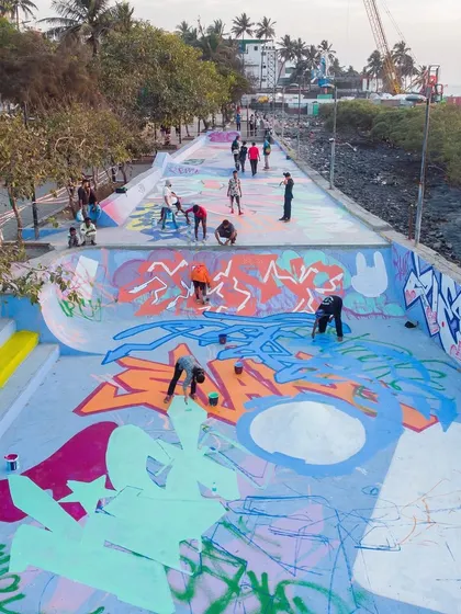 An overhead view of multiple artists painting different sections of the skatepark floor, showing the organized chaos of a large-scale graffiti production.