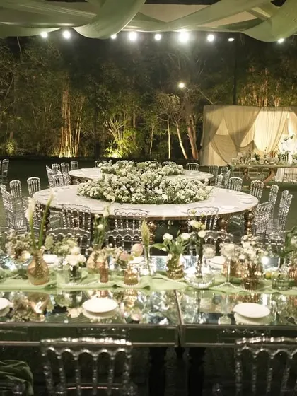 The unique figure-eight dining table, completely covered in white florals, is a stunning centerpiece for this outdoor reception.