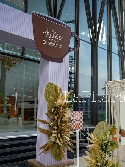 A detail shot of the entrance decor, showing the custom coffee cup cutout, pampas grass arrangements, and a macrame welcome board.