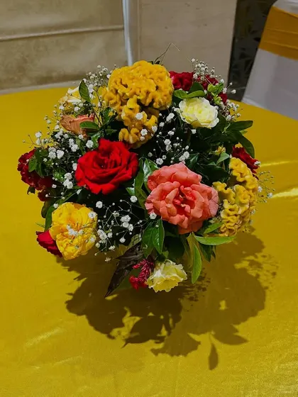 A close-up of a vibrant floral centerpiece for a table, using a mix of red, yellow, and pink flowers to add color to the setting.