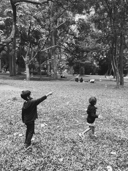A black and white photo of children chasing giant bubbles in the park. This captures a timeless moment of childhood joy, a frequent sight at Cubbon Tales.