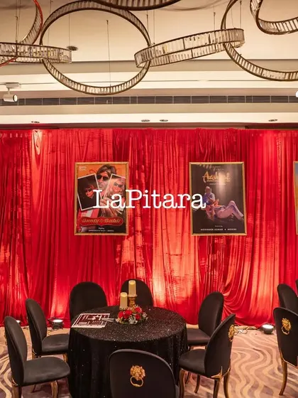 The dining area for the Bollywood party, featuring black sequined tablecloths and chairs with gold lion-head details, set against the red velvet movie poster wall.