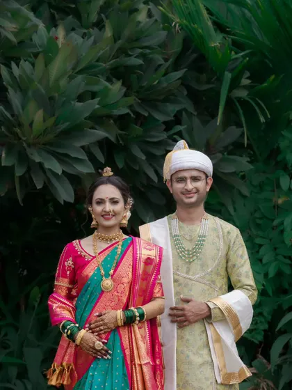 A classic formal portrait of the Maharashtrian wedding couple, their vibrant traditional outfits standing out against a dark green background.